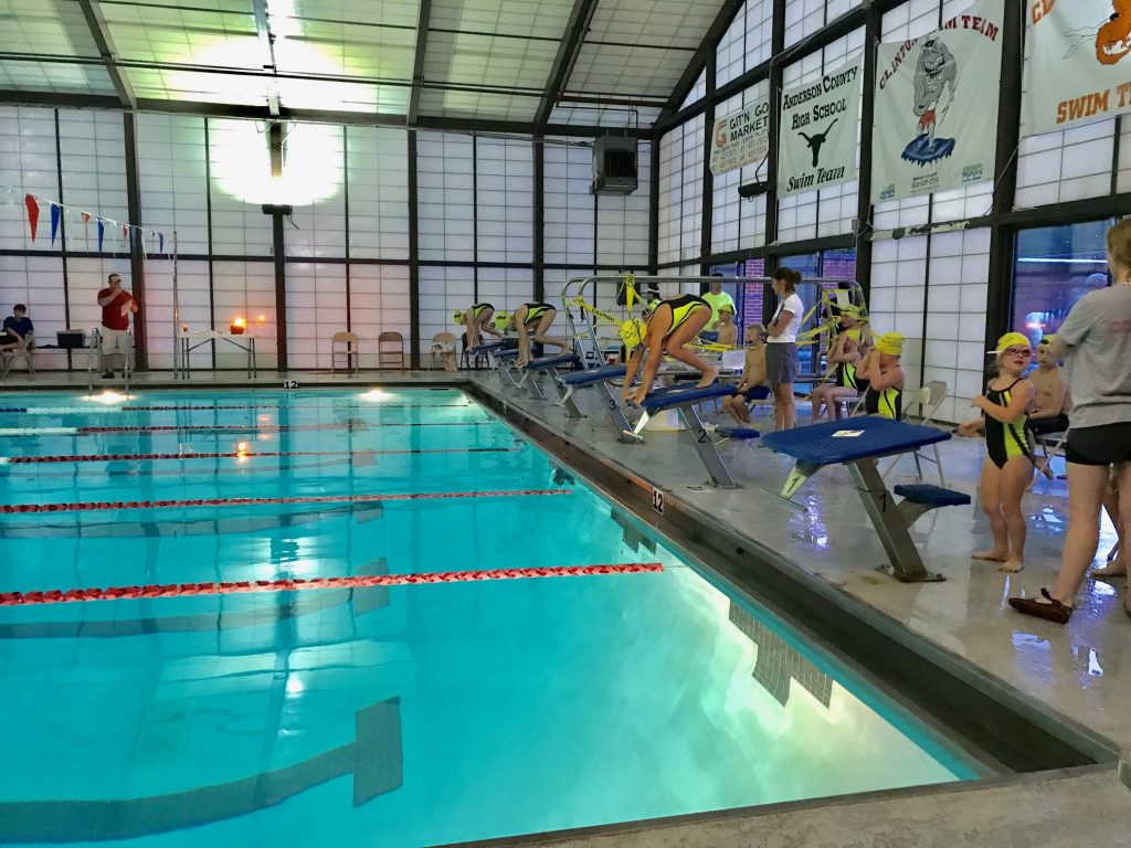 Swim team swimmers standing beside indoor pool